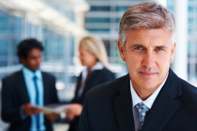 PEO Businessman looking at the camera with other employees talking in the back